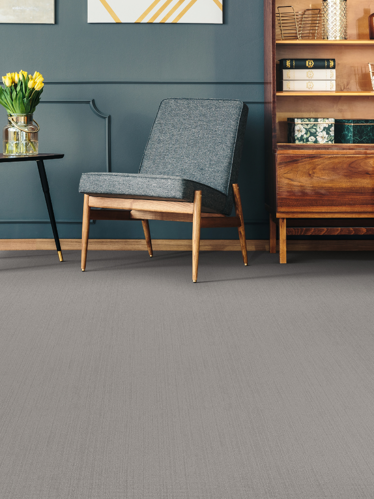 Grey carpet, blue/grey chair, side black table with yellow flowers, wood cabinet.
